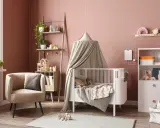 Une chambre bébé DIY chaleureuse avec un lit blanc, un fauteuil confortable, une étagère murale décorée et des jouets en bois.
