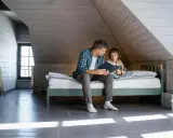 Père lisant une histoire à son fils sur un lit sous pente, dans une chambre mansardée.
