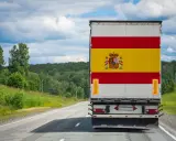 Camion aux couleurs de l'Espagne sur une route de campagne, prêt à déménager en Espagne. Paysage verdoyant sous un ciel nuageux.