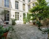 Cour pavée d'un immeuble parisien, avec un petit olivier et une table. Idéal pour un projet de déménager à Paris et profiter de la douceur de vivre.