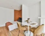 Idée pour aménager studio 30m2 en 2 pièces : un coin nuit cosy avec lit et tête de lit ocre, séparé par une table ronde et des fauteuils velours.