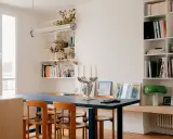 Salle à manger lumineuse d'un appartement traversant, avec table bleue, chaises en bois et étagères remplies de livres.