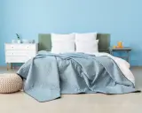 Une chambre paisible avec un lit douillet recouvert d'une couverture bleu glacier. Un pouf moelleux et une commode blanche complètent l'ensemble.