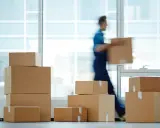 Un déménageur porte une boîte, entouré de cartons empilés. Une scène typique pour une facture déménagement.