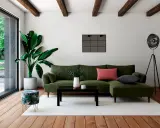 Un salon moderne avec un canapé vert, une table basse noire et un pouf décoré de feuilles tropicales. Quel meuble devant baie vitrée ? Le pouf, parfait pour un coin lecture.