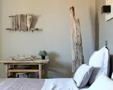 Idée pour comment décorer une chambre : un lit douillet, une table en bois brut, une plante verte et une sculpture murale en bois flotté.