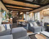Salon cosy d'une maison de pêcheur rénovée, avec canapés gris, table en bois, murs en pierre et plantes vertes.