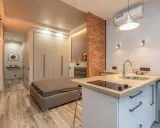 Aménagement studio 25 m2 : lit, cuisine équipée, rangements intégrés, mur en briques apparentes. Style moderne et fonctionnel.