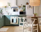 Cuisine verte avec four blanc, îlot central en bois et chaises blanches. Un modèle de cuisine simple et chaleureux.