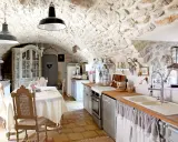 Cuisine rustique avec des vieux meubles patinés, un buffet ancien, une table dressée et des murs en pierre.