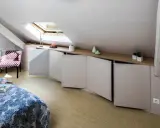 Chambre mansardée d'un coté avec lit, fauteuil à pois et rangements bas sur mesure. Un velux éclaire la pièce.