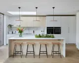 Élégante cuisine ouverte avec îlot central, tabourets en bois, et un jardin d'herbes aromatiques. Des armoires blanches et des fours intégrés complètent ce design moderne.