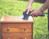 Préparation d'un meuble en bois : ponçage pour comment décaper un meuble en bois foncé. L'outil électrique enlève l'ancienne finition.