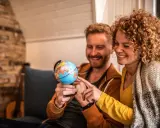 Couple souriant planifiant leur déménagement à l'étranger, pointant du doigt un globe terrestre.