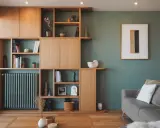 Agencement bibliothèque en bois clair, avec des étagères remplies de livres, vases et objets décoratifs. Un radiateur vert s'intègre parfaitement.