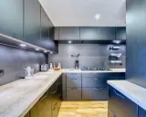 Cuisine moderne aux armoires sombres et plans de travail en bois. Une plaque de cuisson est installée, créant une cuisine sans hotte visible.