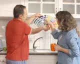 Un couple choisit des couleurs pour peindre le carrelage de sa cuisine, tenant un éventail de nuanciers.