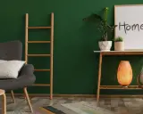 Un salon cosy avec un mur vert sapin, un fauteuil gris, une échelle en bois, une plante et un cadre "Home".