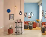 Salon aux murs bleu ciel et rose poudré, mobilier orange vif, tapis jaune moutarde et accents de **couleur pastel**.