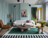 Un salon moderne avec un canapé blanc bouclé, un fauteuil en cuir marron, une table basse ronde et un tapis graphique. Une décoration appartement audacieuse et colorée.