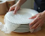 Mains protègent une pile de vaisselle avec du papier bulle, préparant le déménagement.