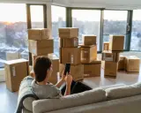 Une femme sur un canapé regarde son téléphone, entourée de cartons. Elle prépare son déménagement à Lyon.
