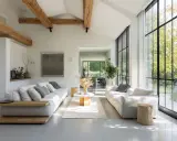 Salon lumineux avec poutres apparentes, rappelant l'esprit d'une maison hangar. Deux canapés blancs font face à une grande baie vitrée.