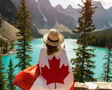 Vue d'une femme avec un drapeau canadien sur les épaules, contemplant un lac turquoise et des montagnes. Un rêve de déménagement France Canada.