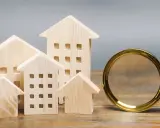 Maquettes de maisons en bois et une loupe, symbolisant la recherche pour trouver un logement rapidement.