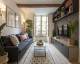 Salon cosy dans une maison en longueur, avec un canapé bleu, une table basse, une TV et des étagères.