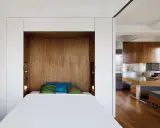 Un petit espace chambre salon optimisé avec un lit escamotable en bois, des coussins colorés et une cuisine moderne adjacente.