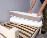 Un homme montre comment plier un matelas sur un sommier en bois.