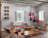 Salon d'une typique maison grecque avec mobilier en bois, tapis coloré et vue sur la mer par la fenêtre.