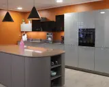 Un exemple de cuisine moderne aux lignes épurées, avec un îlot central gris et des meubles hauts gris clair. L'orange vif du mur apporte une touche de dynamisme.