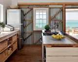 Cuisine campagne chic avec réfrigérateur, plan de travail en bois brut, murs en tôle ondulée et vue sur la mer.