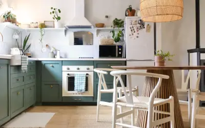 Cuisine verte avec four blanc, îlot central en bois et chaises blanches. Un modèle de cuisine simple et chaleureux.