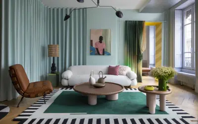 Un salon moderne avec un canapé blanc bouclé, un fauteuil en cuir marron, une table basse ronde et un tapis graphique. Une décoration appartement audacieuse et colorée.