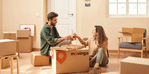 Un couple trinque avec des bouteilles devant une pizza, entouré de cartons. Un avis positif pour Movinga.