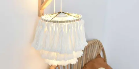 Un abat jour DIY en macramé blanc, avec des franges douces, éclaire une chambre cosy.