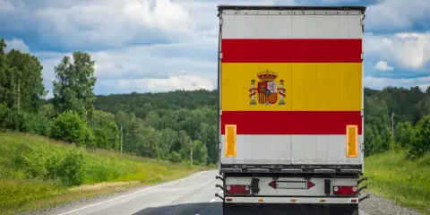 Camion aux couleurs de l'Espagne sur une route de campagne, prêt à déménager en Espagne. Paysage verdoyant sous un ciel nuageux.