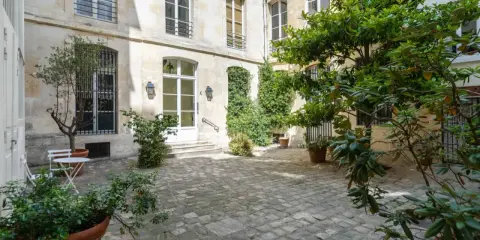 Cour pavée d'un immeuble parisien, avec un petit olivier et une table. Idéal pour un projet de déménager à Paris et profiter de la douceur de vivre.