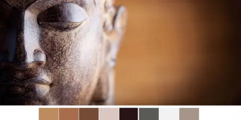 Gros plan sur le visage d'une statue de Bouddha aux tons terreux, avec une palette de couleurs apaisantes.
