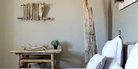 Idée pour comment décorer une chambre : un lit douillet, une table en bois brut, une plante verte et une sculpture murale en bois flotté.