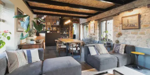 Salon cosy d'une maison de pêcheur rénovée, avec canapés gris, table en bois, murs en pierre et plantes vertes.