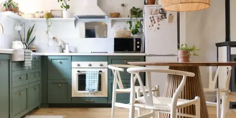 Cuisine verte avec four blanc, îlot central en bois et chaises blanches. Un modèle de cuisine simple et chaleureux.