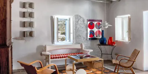 Salon d'une typique maison grecque avec mobilier en bois, tapis coloré et vue sur la mer par la fenêtre.