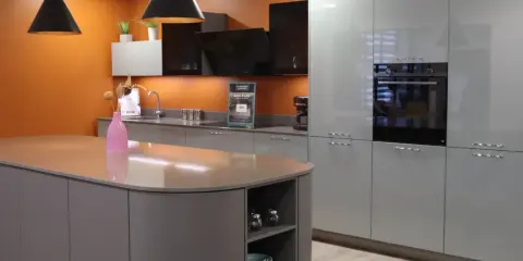Un exemple de cuisine moderne aux lignes épurées, avec un îlot central gris et des meubles hauts gris clair. L'orange vif du mur apporte une touche de dynamisme.