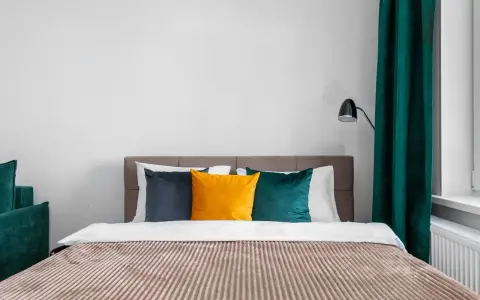 Lit de chambre cabine avec coussins colorés et rideaux verts.