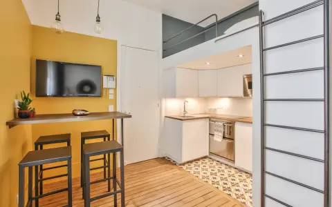 Aménagement studio 18m² : cuisine moderne, coin repas jaune vif avec TV, et lit mezzanine accessible par une échelle.