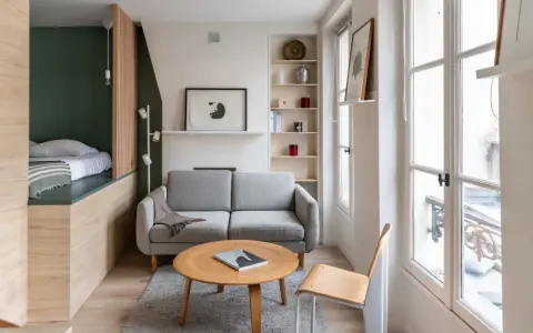 Aménagement intérieur appartement : un salon cosy avec canapé gris, table basse en bois, et un lit surélevé dans un coin.